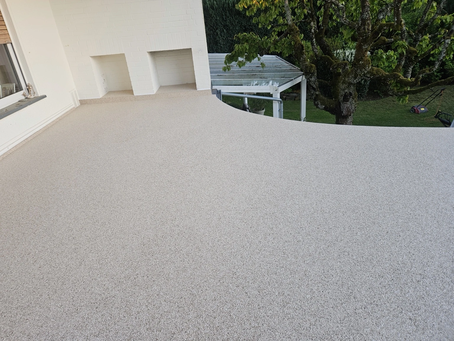 Große helle Terrassenfläche vor weißer Hausfassade und Garten
