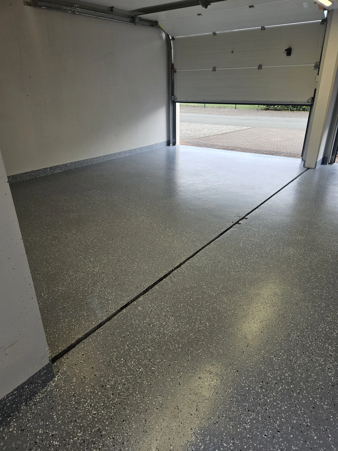 Fertige Garage mit grauer gesprenkelter Bodenfläche und geöffnetem Garagentor