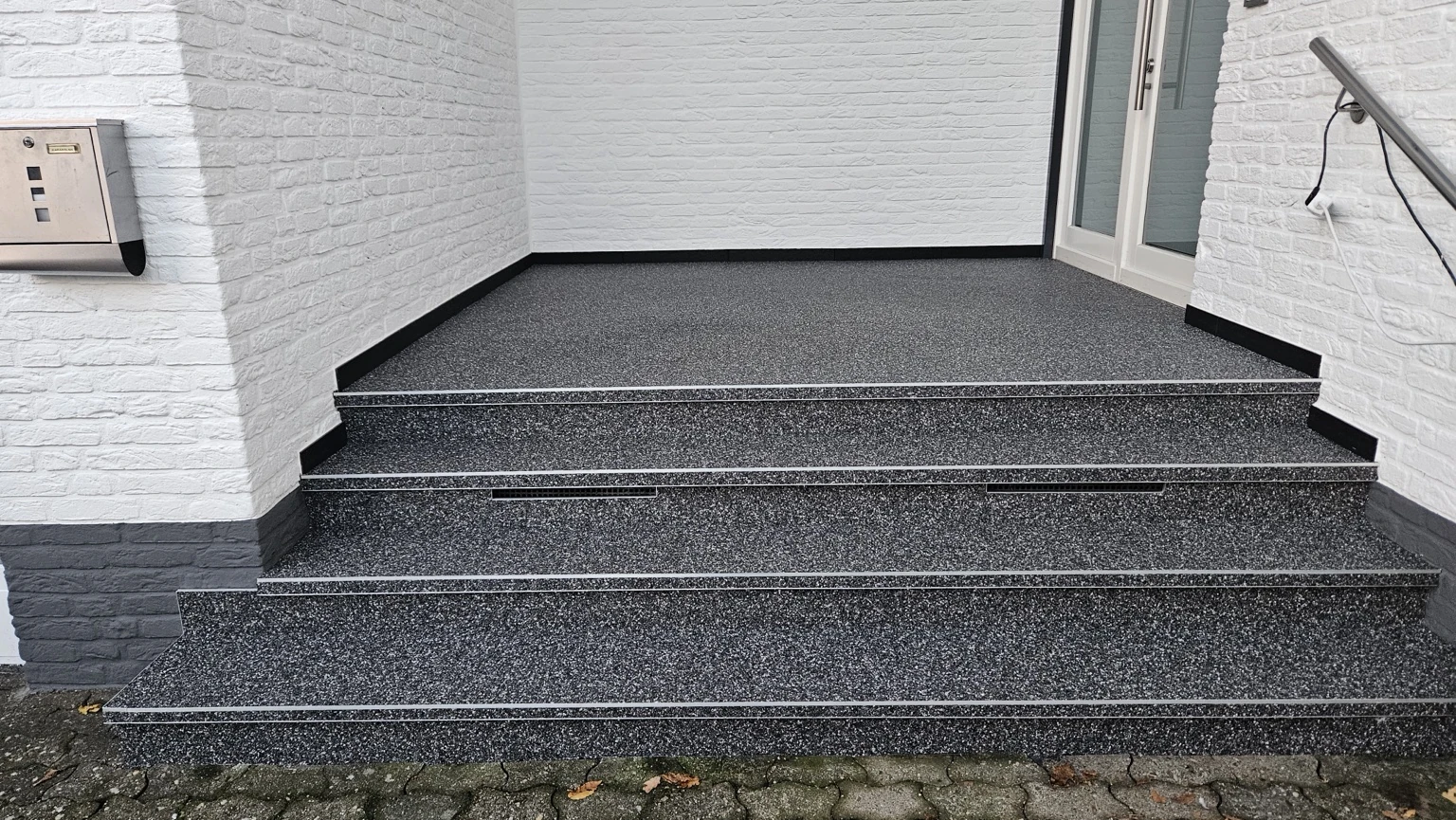 Fertige dunkelgraue Eingangstreppe zwischen weißen Ziegelwänden